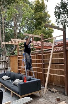 a man is standing on a ladder working on a couch in the back yard area