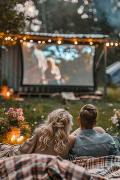 two people sitting on a blanket watching a movie