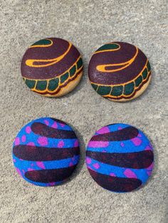 three painted rocks sitting on top of a cement floor next to each other and one has an orange, purple, and blue design