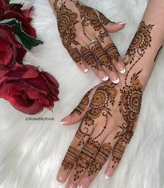 two hands with henna designs on them next to a red rose and white furnishing