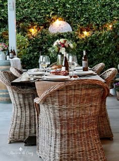 an outdoor dining area with wicker chairs and table set up for two, surrounded by greenery