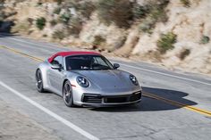 a silver porsche sports car driving down the road with mountains in the backgroud