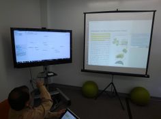 a man sitting at a desk in front of a large screen with two monitors on it