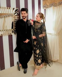 a man and woman standing next to each other in front of a striped wallpapered room