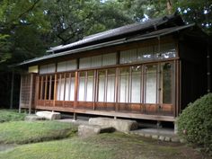 a small wooden building sitting on top of a grass covered field next to trees and bushes