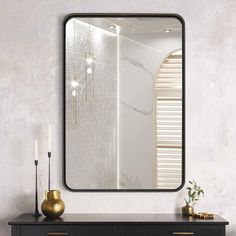 a mirror on a wall above a dresser with a vase and candle in front of it