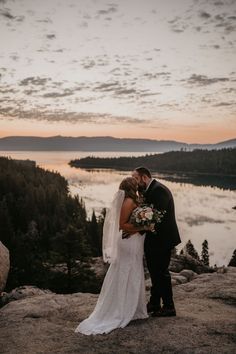 a bride and groom kissing on top of a mountain overlooking the lake at sunset with mountains in the background