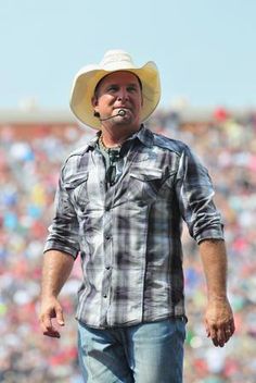 a man wearing a cowboy hat walks on the sidelines in front of a large crowd