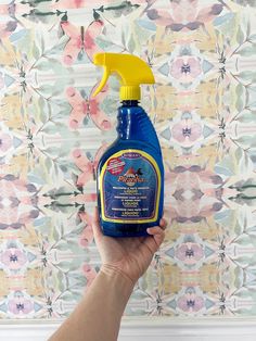 a hand holding a blue bottle of cleaner in front of a wallpapered background