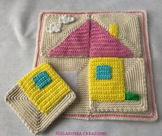 two crocheted coasters are sitting on a white surface with a pink and yellow house