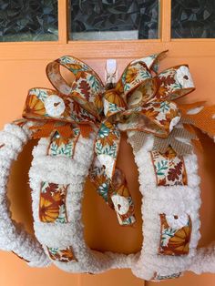 a wreath is hanging on the front door with an orange bow and white pom - poms