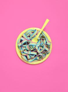 a yellow bowl filled with colorful noodles on top of a pink surface