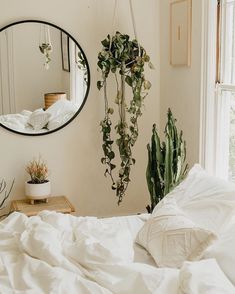 a bed with white sheets and plants hanging from the wall next to a round mirror