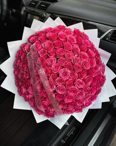 a bouquet of pink roses sitting on the hood of a car with a ribbon around it