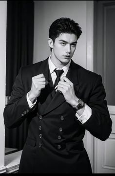 a young man adjusting his tie in a black and white photo by an open door