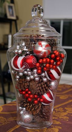 a glass container filled with christmas ornaments and pineconis on top of a table