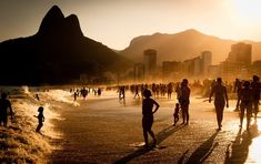 many people are walking on the beach at sunset or sunrise, with mountains in the background