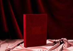 a red book sitting on top of a bed next to a pink cloth covered wall