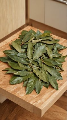 a pile of green leaves sitting on top of a wooden cutting board in a kitchen