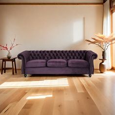 a purple couch sitting on top of a hard wood floor next to a vase filled with flowers