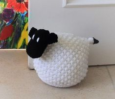 a crocheted sheep sitting in front of a door with a painting behind it