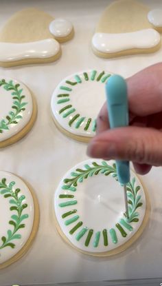 a person is decorating cookies with icing and green leaves on white frosting