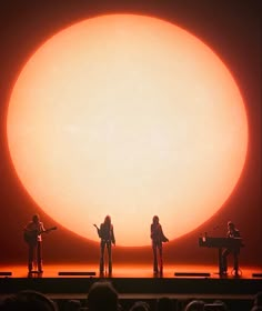 three people standing on stage in front of an orange sun