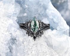 a green and white stone ring sitting on top of some ice floese with black diamond accents