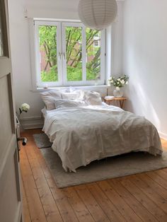 a white bed sitting under a window next to a wooden floor