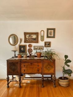 a wooden table topped with potted plants next to a wall filled with framed pictures