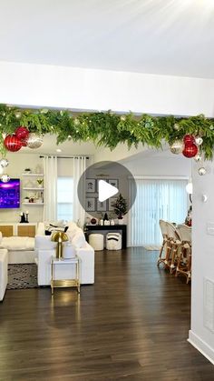 a living room filled with white furniture and christmas decorations hanging from the ceiling over a wooden floor