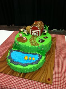 a green cake with farm animals on it sitting on a red and white checkered table cloth