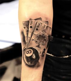 a man with a tattoo on his arm has playing cards and a pool ball in front of him