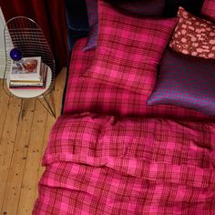 a bed with red and black plaid comforter next to a night stand on the floor