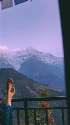 a person laying down on a balcony with their feet in the air and mountains in the background