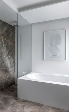 a white bath tub sitting in a bathroom next to a walk in shower and a painting on the wall