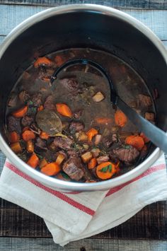 a pot filled with meat and carrots on top of a wooden table next to a white towel