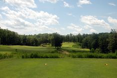 a golf course surrounded by trees on a sunny day with blue skies and white clouds