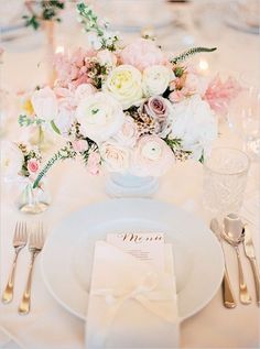 the table is set with white and pink flowers, silverware, and napkins