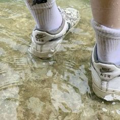 a person standing in shallow water wearing white shoes