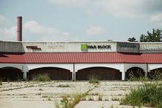 an abandoned building with many windows and red roofing on the top, in front of some grass