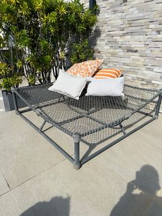 a metal bed frame with two pillows on it and some bushes in the back ground