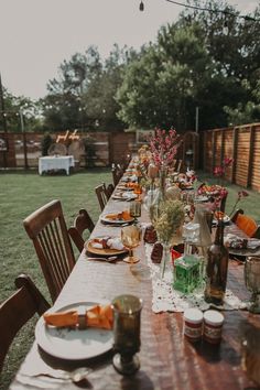 a long wooden table with plates and glasses on top of it in the middle of a yard