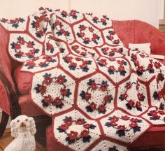 a red couch with a white crocheted blanket on it and a dog sitting next to it