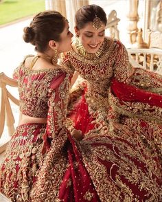 two women in red and gold wedding dresses, one is touching the other's cheek