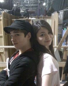 a young man and woman standing next to each other in front of shelves with items on them