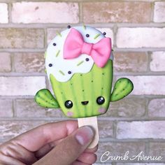 a hand holding a small green cactus with a pink bow on it's head