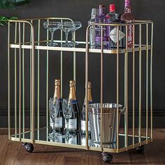 a gold bar cart with bottles and glasses on it next to a potted plant