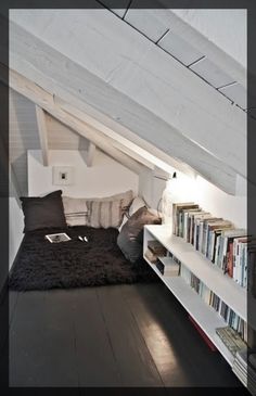 there is a bed in the attic with books on it and a book shelf below