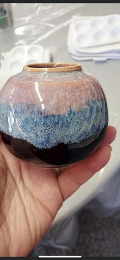 a hand holding a small ceramic vase with blue and white designs on it's side